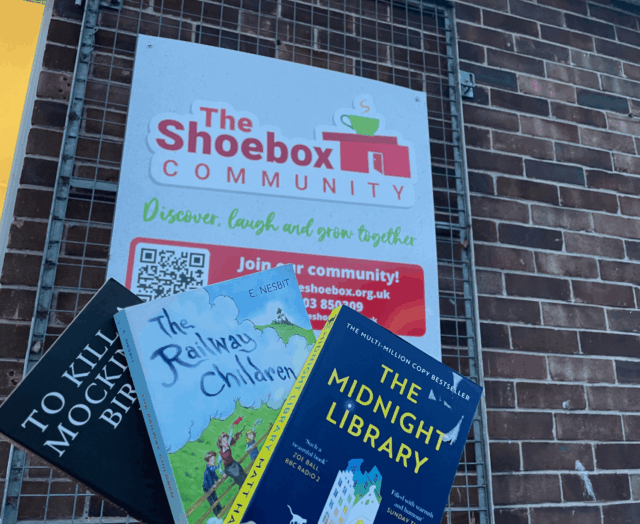 Three books. To kill a mocking bird, the midnight library and the rail way children held up infront of the Shoebox Community sign
